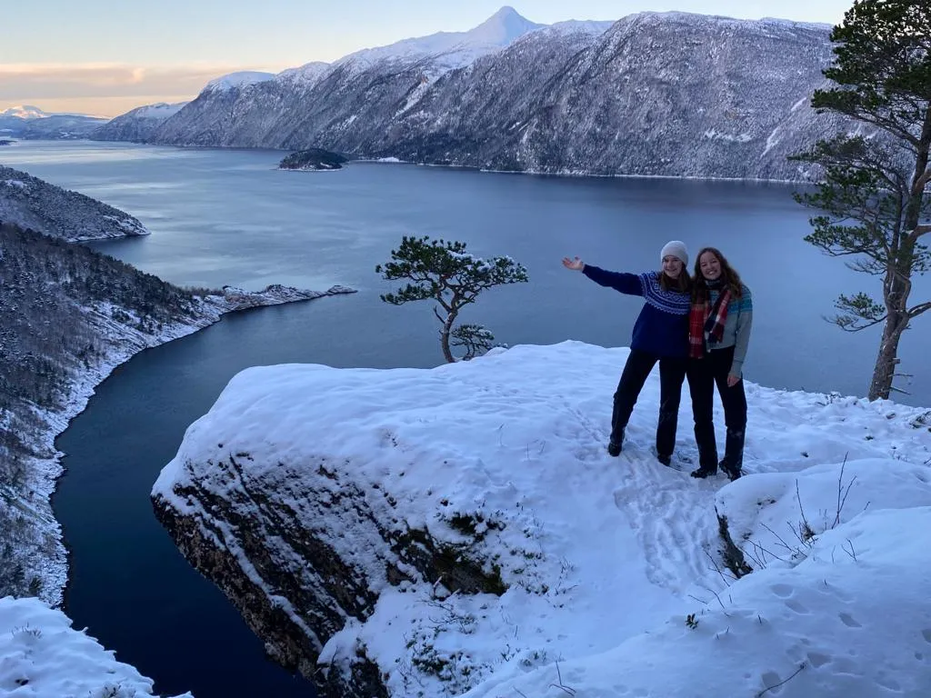 Zwei Schülerinnen posieren über Fjord auf Felsen bei Schnee