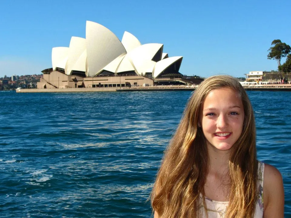 Mädchen steht vor dem Sydney Opernhaus mit Meer dazwischen