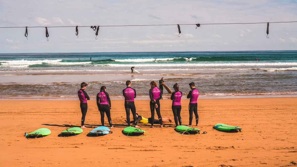 Gruppe Surfer auf rotem Strand mit Wellen im Hintergrund