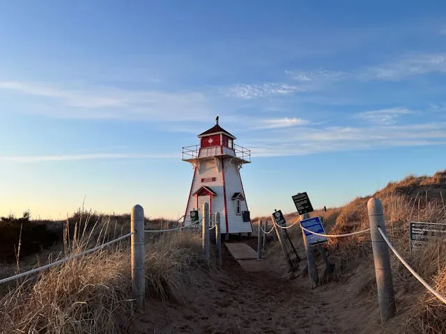 Morgendämmerung bei rot-weissem Leuchtturm zwischen braunen Feldern und blauem Himmel