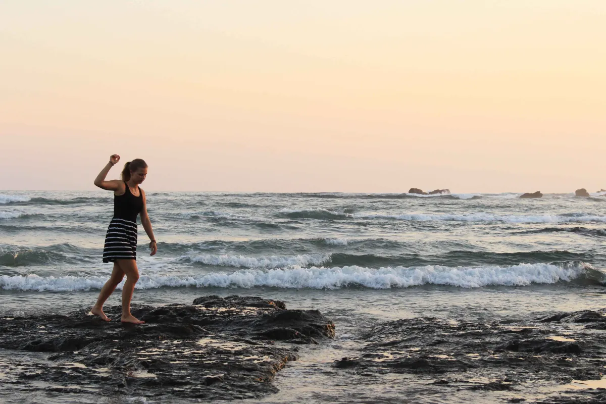 Junge Frau tanzt in Wellen bei Sonnenuntergang am Strand