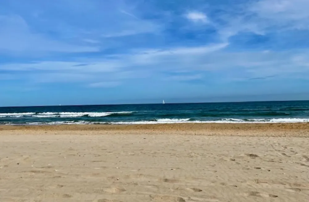 Brauner Sandstrand, weisse kleine Wellen, blauer Himmel