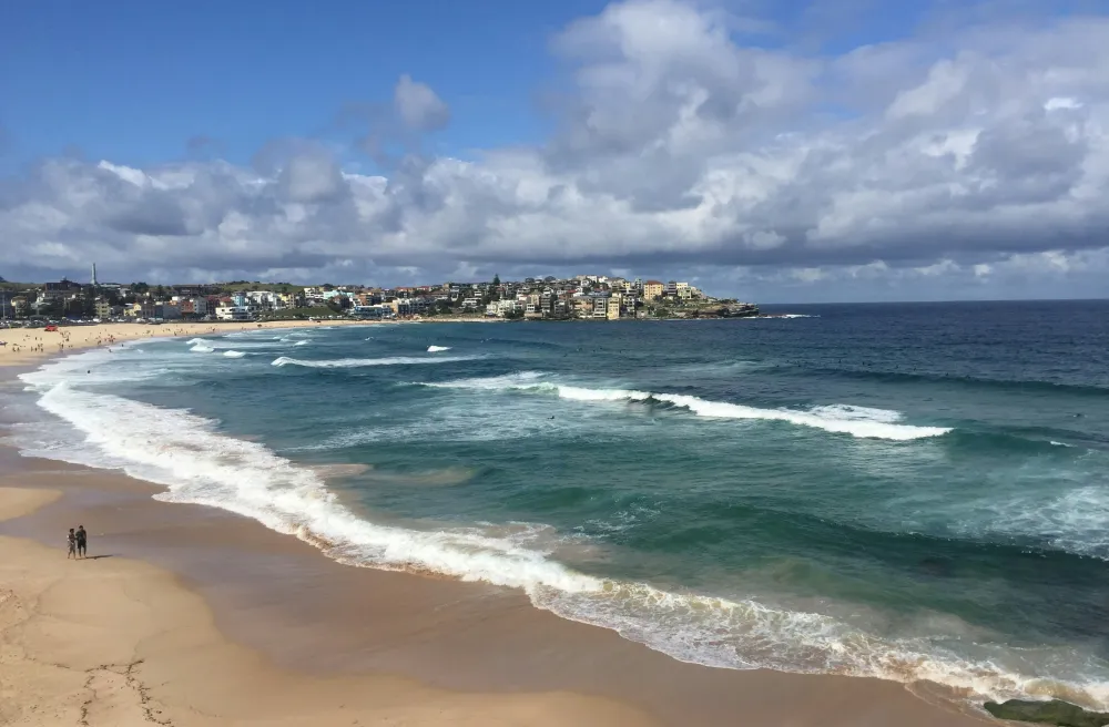 Endloser Strand mit weissen Wellen und Meer mit Wolken