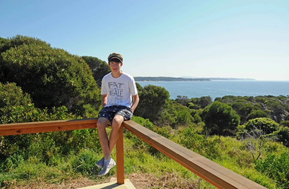 Junge sitzt auf Mauer bei Aussichtspunk über Bäumen und Meer