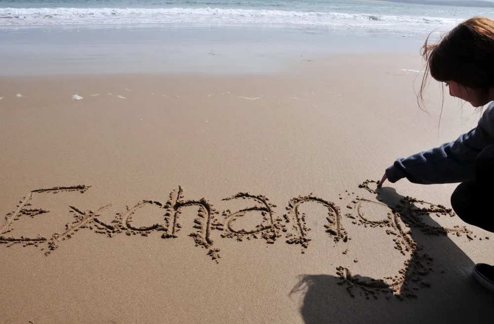 Handschrift im Sand eines Mädchen mit dem Wort Exchange 