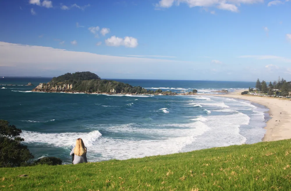 Strand mit weissen Wellen und grüne Wiese davor und sitzendes Mädchen in Wieser