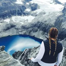 Mädchen von hinten schaut über tiefen Fjord mit Gletscher und grauen Felswänden