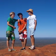 Drei Knaben stehen auf rotem Felsen in Australien mit blauem Himmel