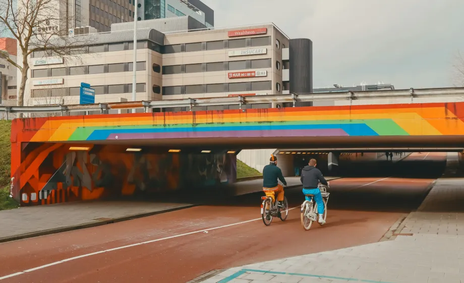 Fahrradweg mit zwei Fahrradfahrer unter Brücke mit Pridefarben
