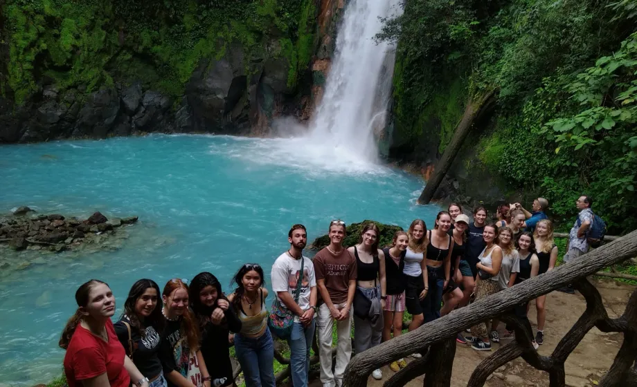 Gruppe Schüler posiert vor Wasserfall und See im Dschungel