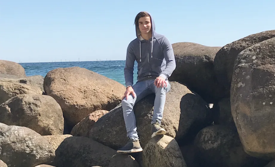 Junge sitzt auf Felsen am Meer mit Hoodie und Kaputze