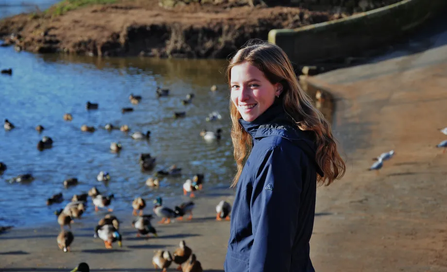 Mädchen in blauer Herbstjacke am See mit vielen Enten