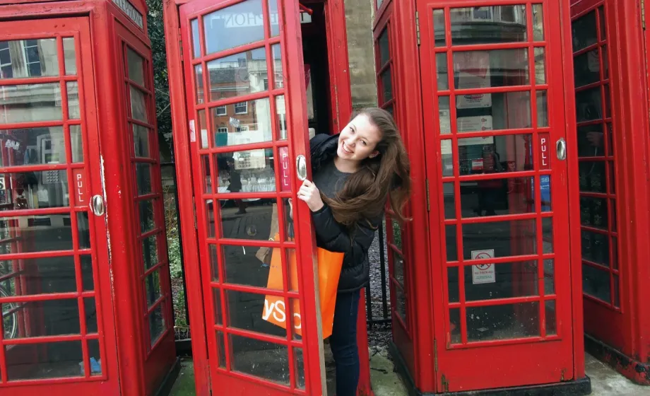Mädchen schaut aus roter Telefonkabine in England raus und lacht