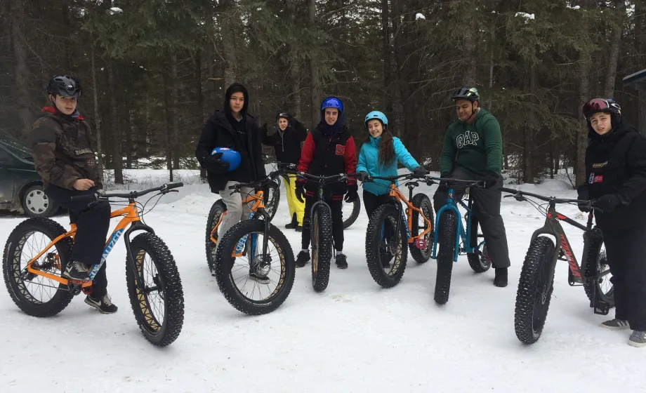 Schüler auf Fatbikes auf Schnee vor Wald