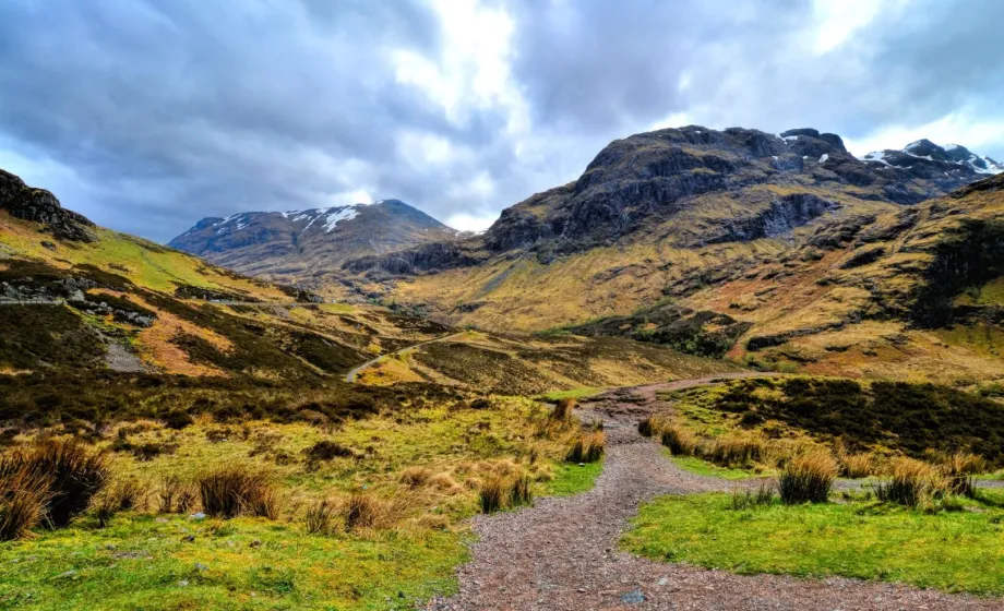 Wanderweg durch schottisches Hochland, gelbe Weiden und schwarze Felsen und Berge mit Wolkenspiel
