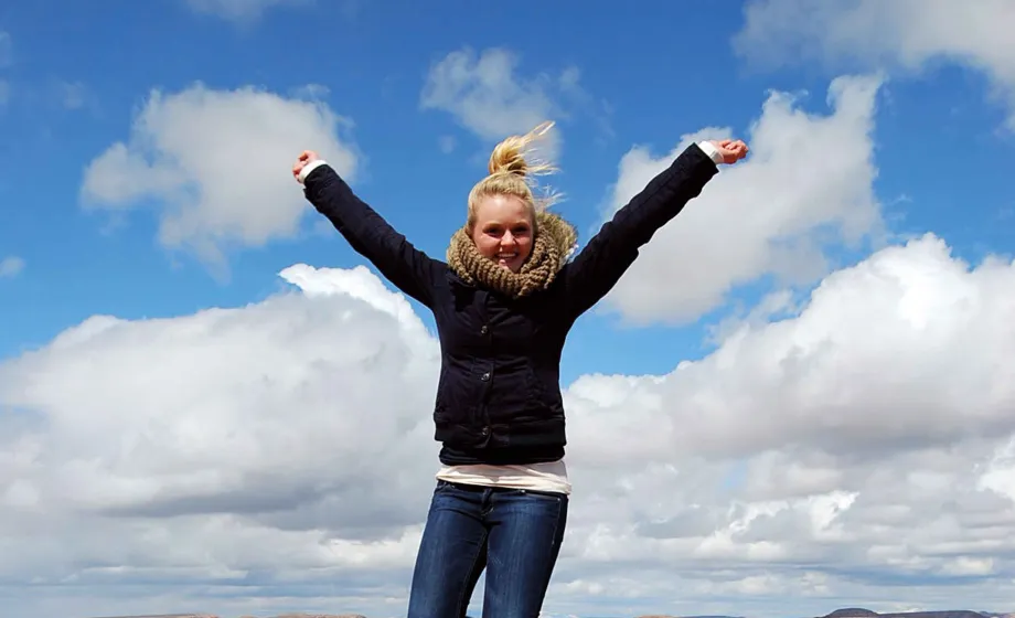 Junge Frau springend in Utha auf roten Felsen mit blauem Himmel
