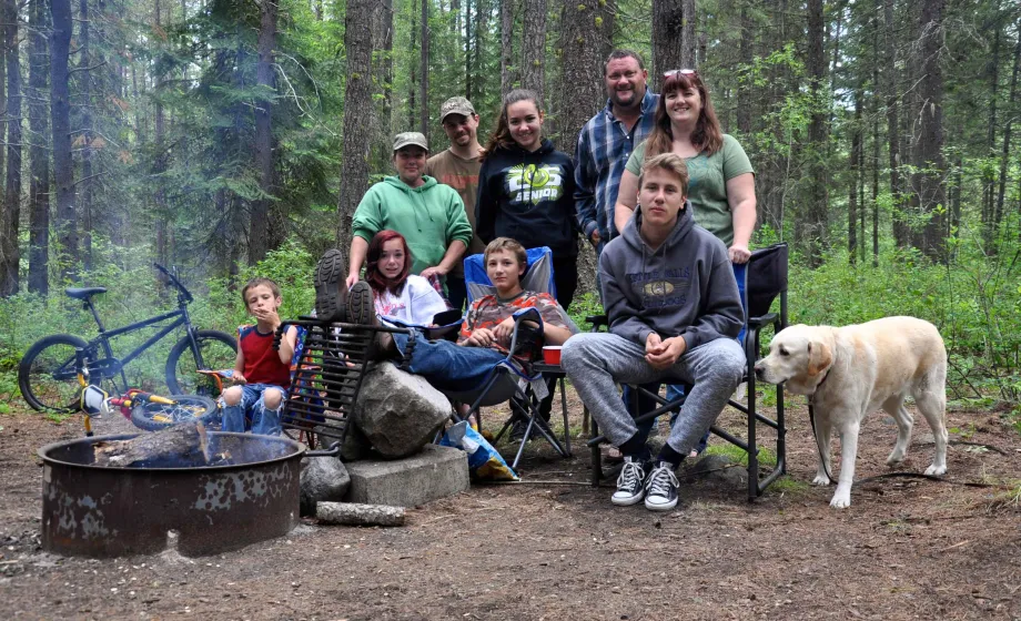 Familie mit Hund an Feuerstelle auf Campingplatz im Wald