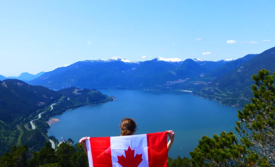 Frau mit Kanada Flagge steht auf Berg mit Seeblick